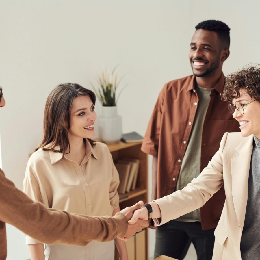 pexels-photo-3184416-3184416 Four colleagues smiling and shaking hands in a bright office setting.