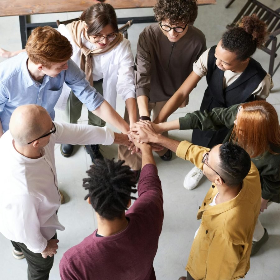 pexels-photo-3184423-3184423 A diverse group of professionals joins hands in a team-building exercise indoors.